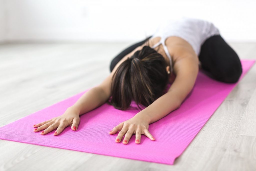 woman performing child's pose in yoga on a pink mat